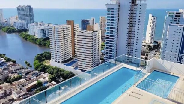 A high-rise building with a rooftop pool overlooking a body of water and a cityscape.