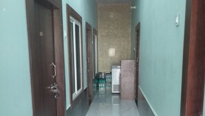 Un couloir avec un sol en marbre, des portes en bois et un réfrigérateur au fond.
