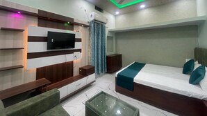 Une chambre d’hôtel moderne, équipée d’un lit, d’un téléviseur fixé au mur, d’un ventilateur de plafond et d’une table basse en verre.
