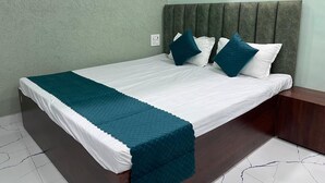 Un lit bien fait, recouvert d’une couvre-lit blanche et turquoise, avec une tête de lit sombre et une table de chevet en bois à côté.