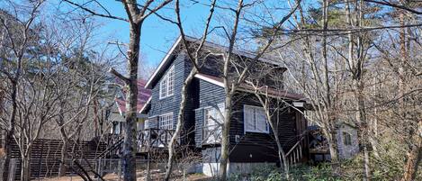A two-story house with a dark exterior, surrounded by trees and a fence.