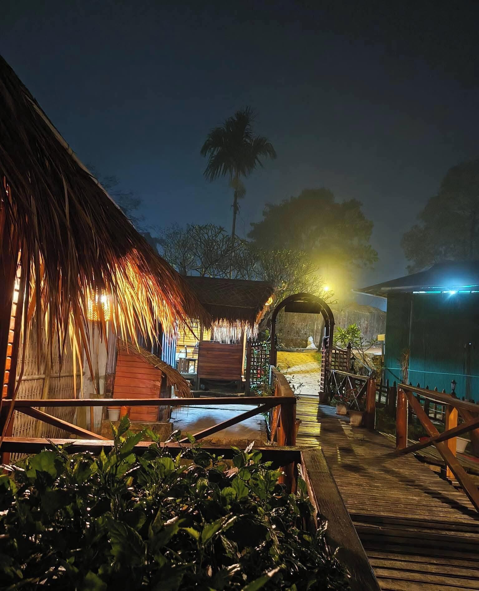 Une terrasse en bois mène à un bâtiment dont le toit est recouvert de chaume, et qui est agrémenté d’une piscine.