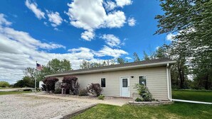 A single-story house with a front door, a small porch, and a flag. - Peaceful Guest House Beside The Elks Golf Course – A Relaxing Country Getaway (Kearney)