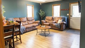 A living room with two leather sofas, a wooden coffee table, and a dining area with a wooden table and chairs. - Peaceful Guest House Beside The Elks Golf Course – A Relaxing Country Getaway (Kearney)