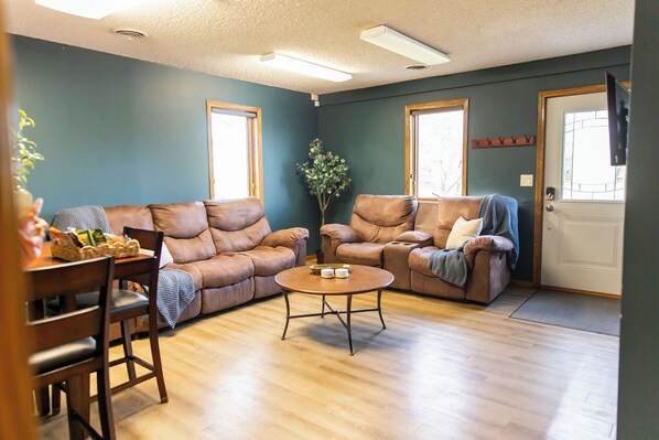 A living room with two leather sofas, a wooden coffee table, and a dining area with a wooden table and chairs.