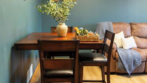 A dining area with a wooden table, two chairs, a vase with green plants, and a basket of snacks. - Peaceful Guest House Beside The Elks Golf Course – A Relaxing Country Getaway (Kearney)