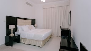 Quarto de hotel com uma cama grande, mesa de cabeceira com luminária, televisão e janela com cortinas.