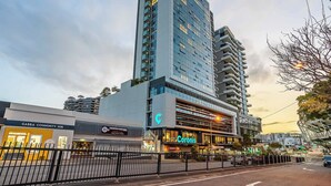 Un hotel moderno con varios pisos, un llamativo letrero de 'Coronis' y el 'Gabba Community Hub' ubicado a su lado.