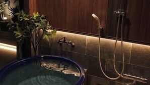 A spa area with a hot tub, shower, and wooden stool. - Kanazawaya Motogikucho (Kanazawa)