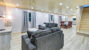 A spacious living area with a large grey sectional sofa, a dining table with chairs, and a kitchen area in the background. - Direct Trail Access: Lyons Falls Getaway w/ Views! (Lyons Falls)