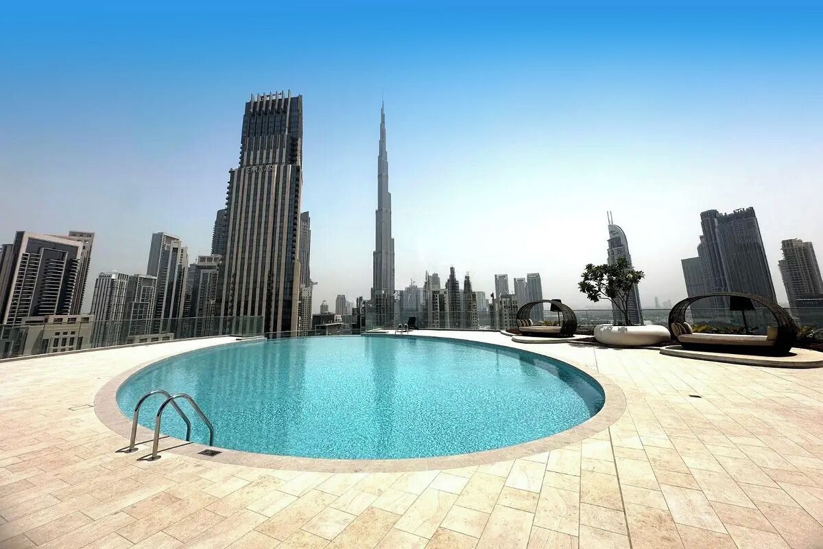 A rooftop swimming pool with a city skyline view, including tall buildings and a clear sky.