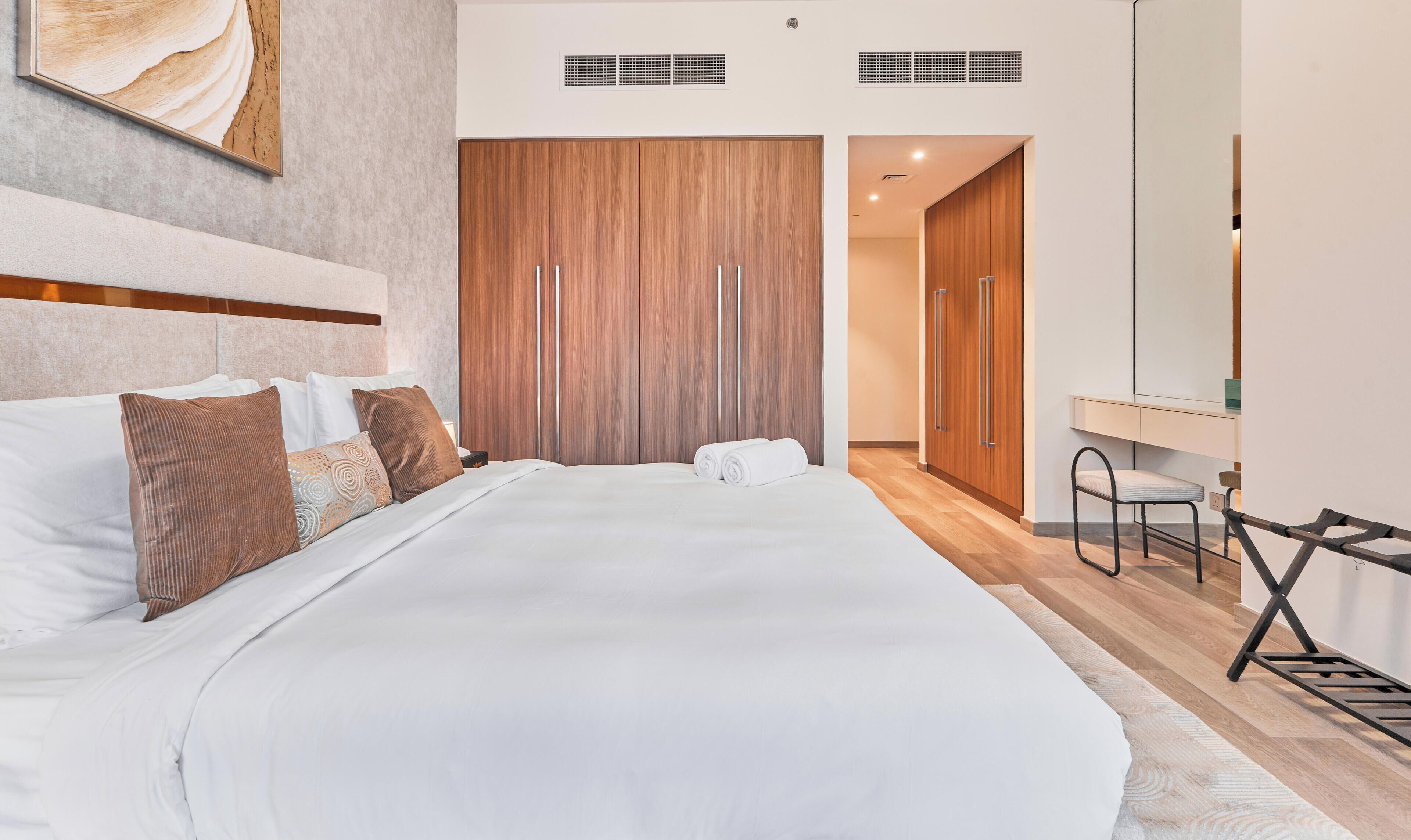 Ein modernes Hotelzimmer mit einem großen Bett, einem Holzschrank, einem Schreibtisch mit Stuhl und einem großen Spiegel.