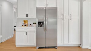 A modern kitchen with white cabinetry, a stainless steel refrigerator, and a wooden floor.