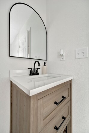 A bathroom with a white sink, black faucet, and wooden cabinet drawers.