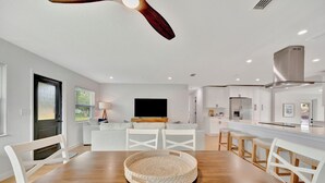 A modern kitchen with white cabinetry, a wooden dining table, and a ceiling fan.