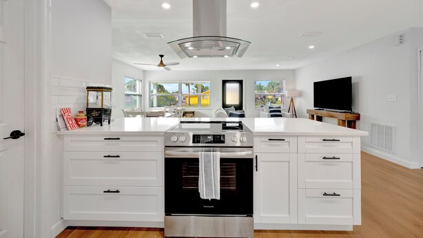 A modern kitchen with white cabinetry, a stainless steel range hood, and a large island with a built-in oven.