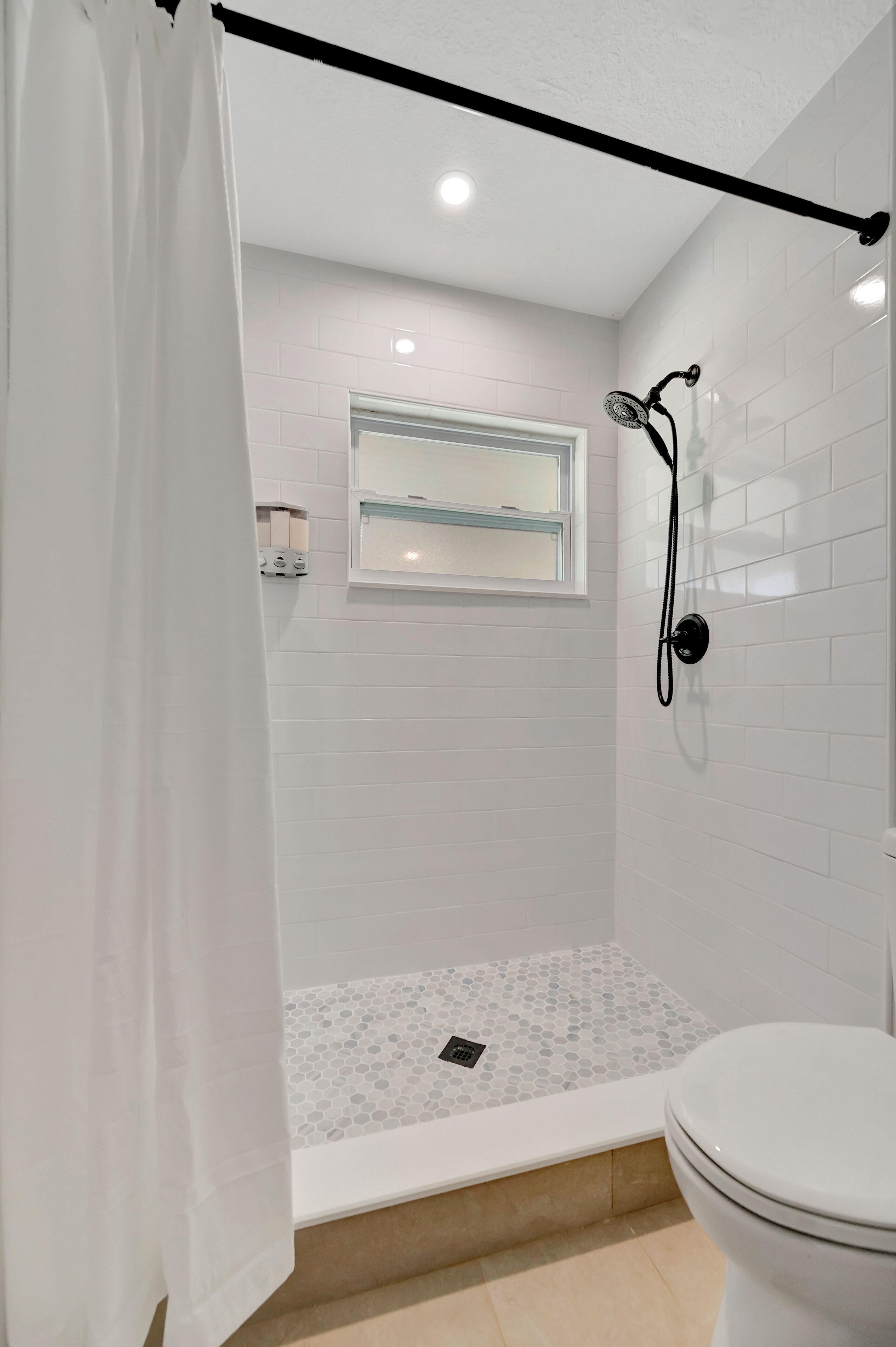 A bathroom with a shower, toilet, and a window.