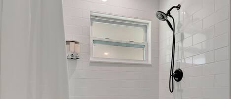 A bathroom with a shower, toilet, and a window.
