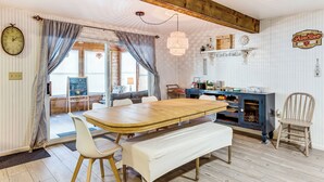 A dining area with a wooden table, white bench, and chairs. There is a blue cabinet with a shelf above the table. - Todd Lake Home: Fish, Snowmobile & Golf! (Reed City)