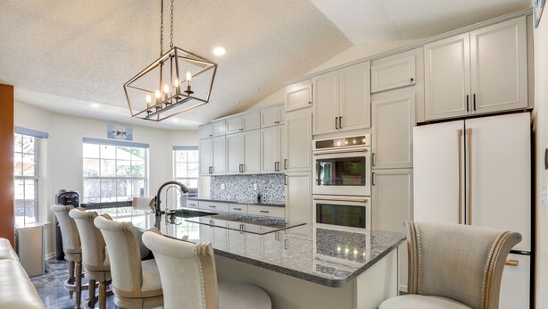 A modern kitchen with white cabinetry, a granite countertop, and a central island with bar stools. - Backyard Oasis w/ Private Pool: Jacksonville Gem (Jacksonville)