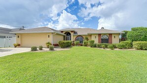 A two-story house with a garage, a well-maintained lawn, and a clear sky. - Waterfront Cape Coral Home: Views & Birdwatching (Cape Coral)