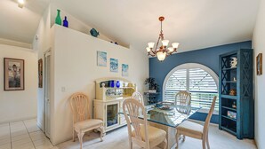A dining area with a glass table, four chairs, a chandelier, and a view through a large arched window. - Waterfront Cape Coral Home: Views & Birdwatching (Cape Coral)