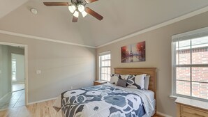 Une chambre avec un grand lit, un ventilateur de plafond, une fenêtre avec des stores et un tableau au mur.