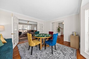 Una sala de estar con una mesa de póker de fieltro verde, cuatro sillas, un sillón azul, un sofá color turquesa y una alfombra estampada.