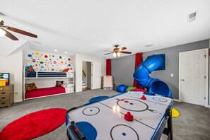 Un cuarto de juegos infantil con una litera, un tobogán y una mesa de hockey.