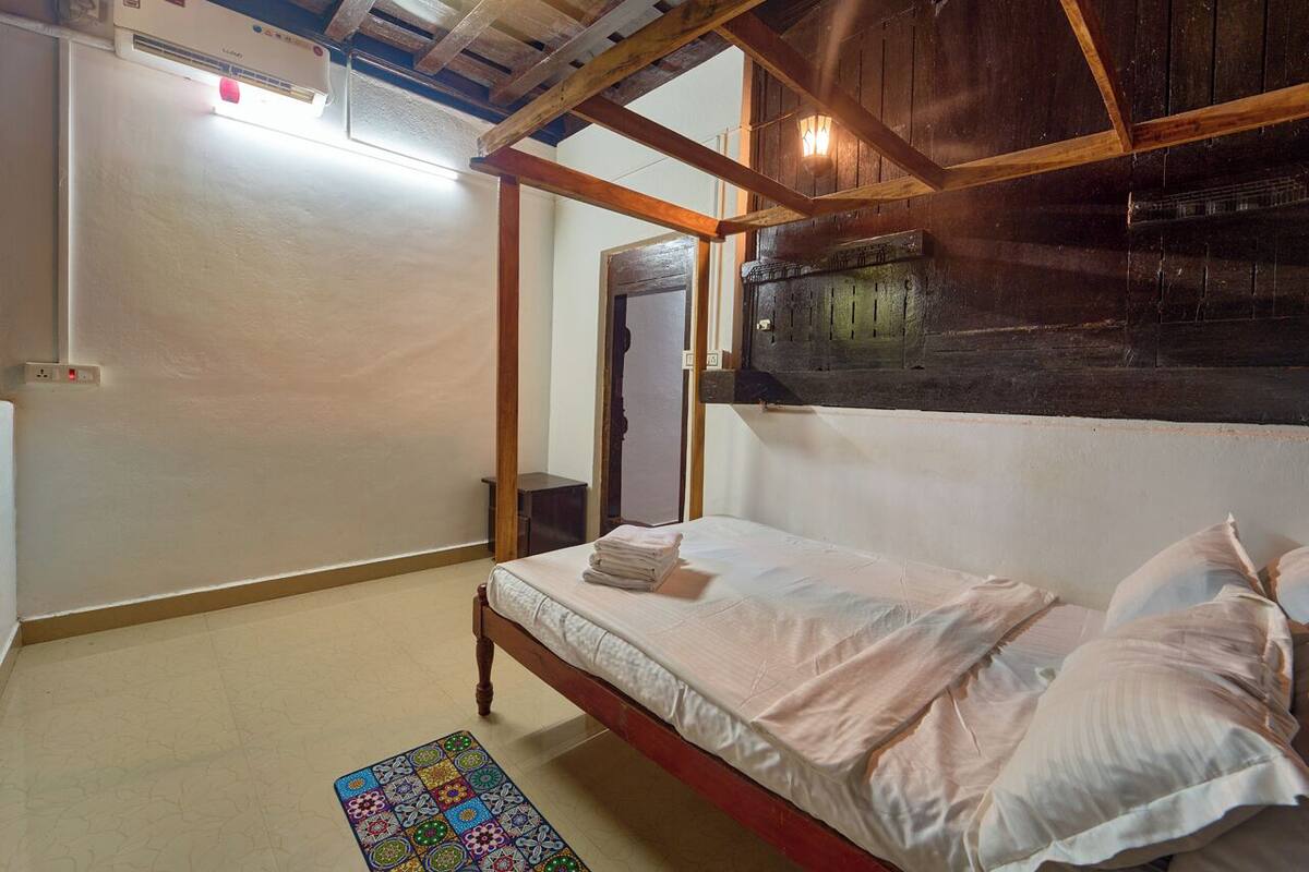 A room with a wooden ceiling, a bed with white linens, a colorful rug, and a small table.