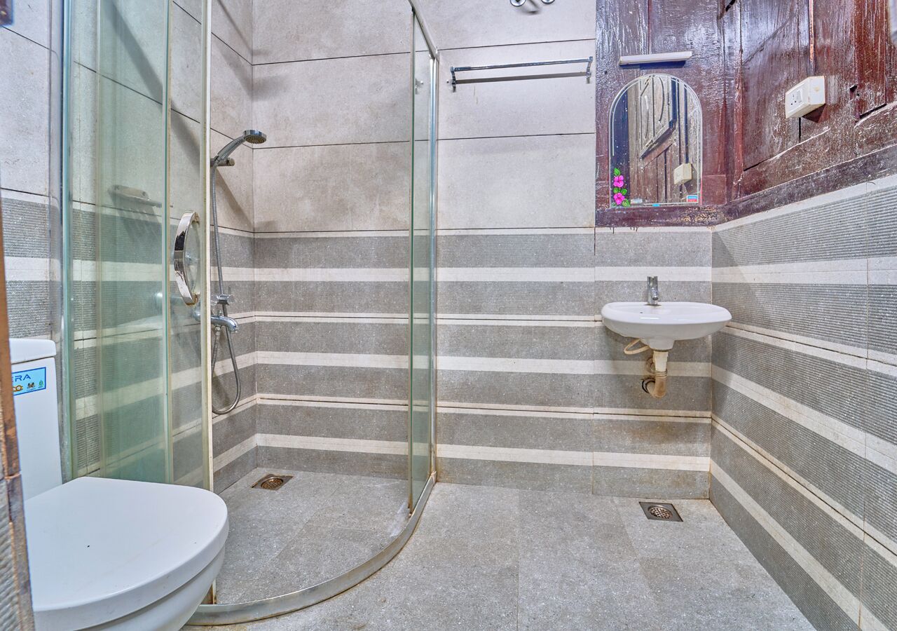 Un baño con cabina de ducha de vidrio, un lavabo blanco y paredes con azulejos a rayas.