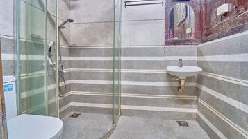 Un baño con cabina de ducha de vidrio, un lavabo blanco y paredes con azulejos a rayas.
