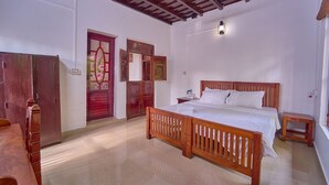 A room with a wooden bed, a small bedside table, a wooden wardrobe, and a red door. - Cotelac Heritage Lake Resort Alleppey (Kuttanad Taluk)