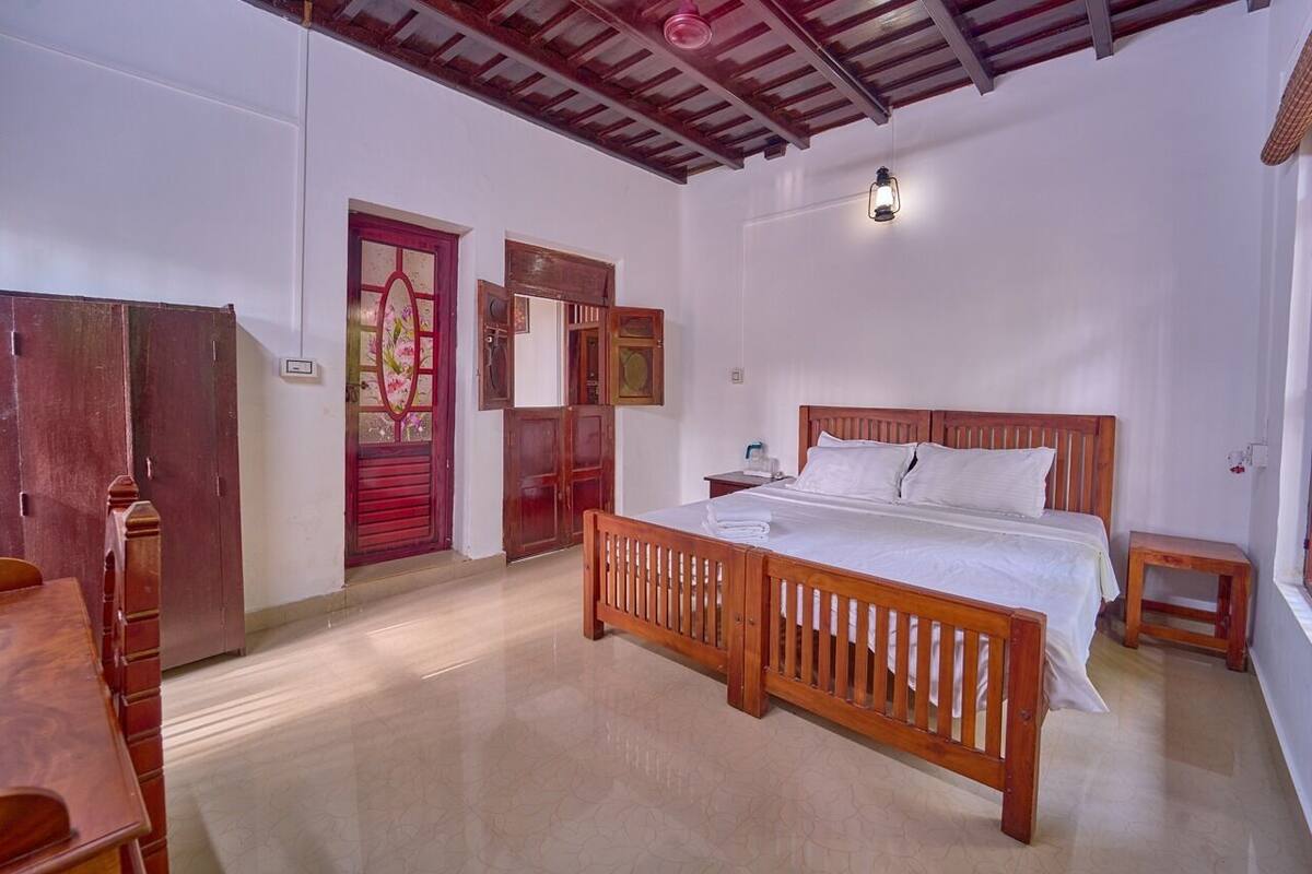 A room with a wooden bed, a small bedside table, a wooden wardrobe, and a red door.