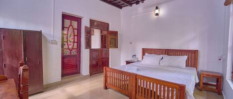 A bedroom with a wooden bed, a nightstand, a wooden table, and a red door.