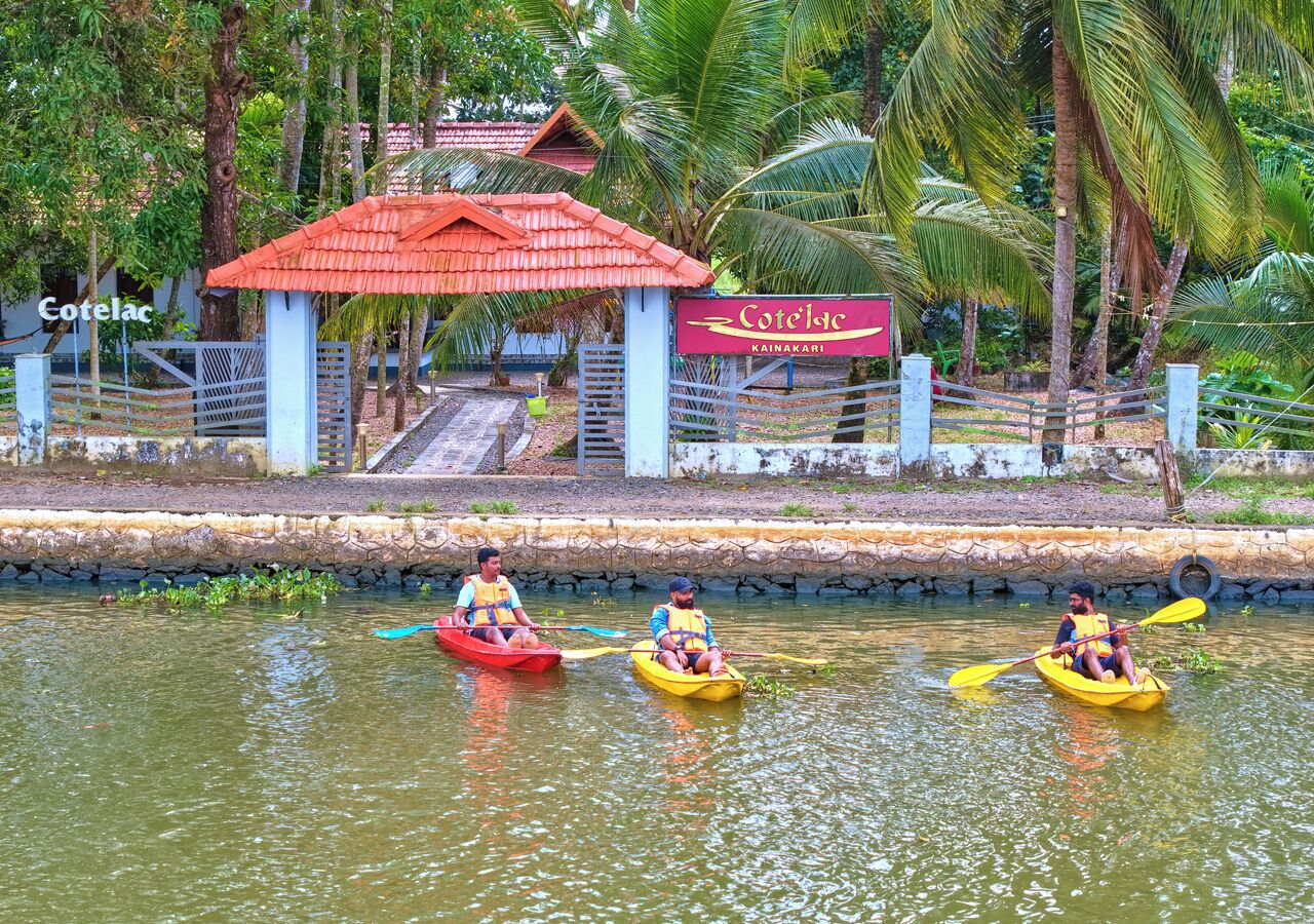 Trois kayaks sur une étendue d’eau calme, avec une structure dotée d’un toit rouge et une enseigne indiquant « Cotelac Kainakari » en arrière-plan.