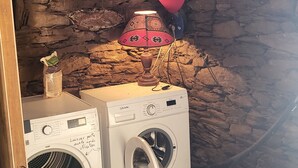 A laundry area with two washing machines, a red lamp, and a stone wall. - THE CHESTNUT TREE HOUSE (Cassagnoles)