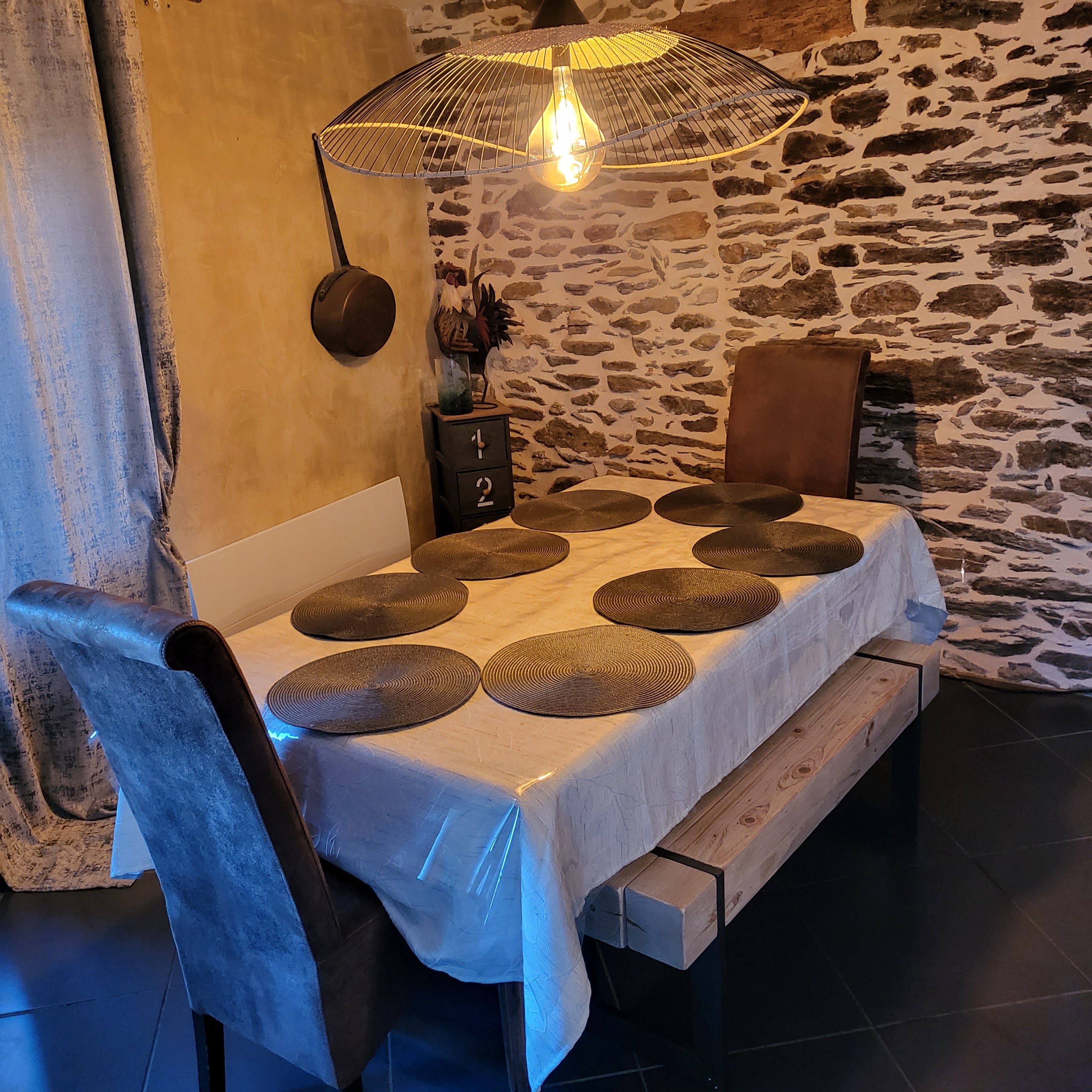 A dining area with a stone wall, a table with round placemats, a hanging light fixture, and a small side table with a number lock.