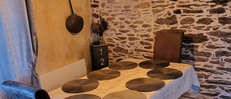 A dining area with a stone wall, a table with round placemats, a hanging light fixture, and a small side table with a number lock.