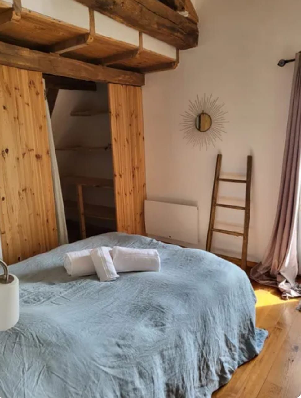 A bedroom with a bed, wooden beams, a ladder, and a wall-mounted sun decoration.