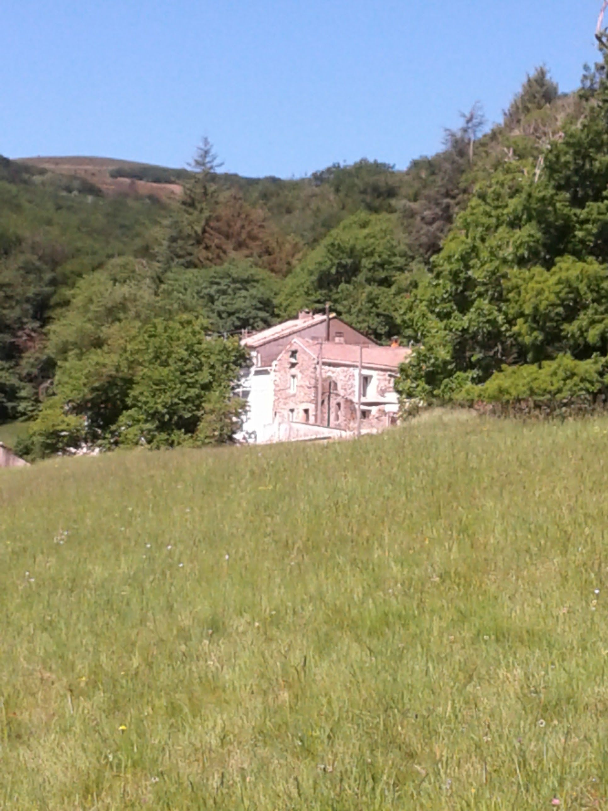 A stone building with a red roof, surrounded by lush greenery and hills.