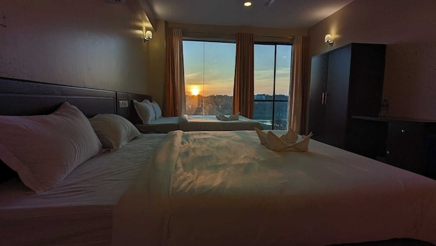 A hotel room with a large bed, a sofa, and a view of the sunset through the window. - Hotel Opera Ocean (Cox's Bazar)