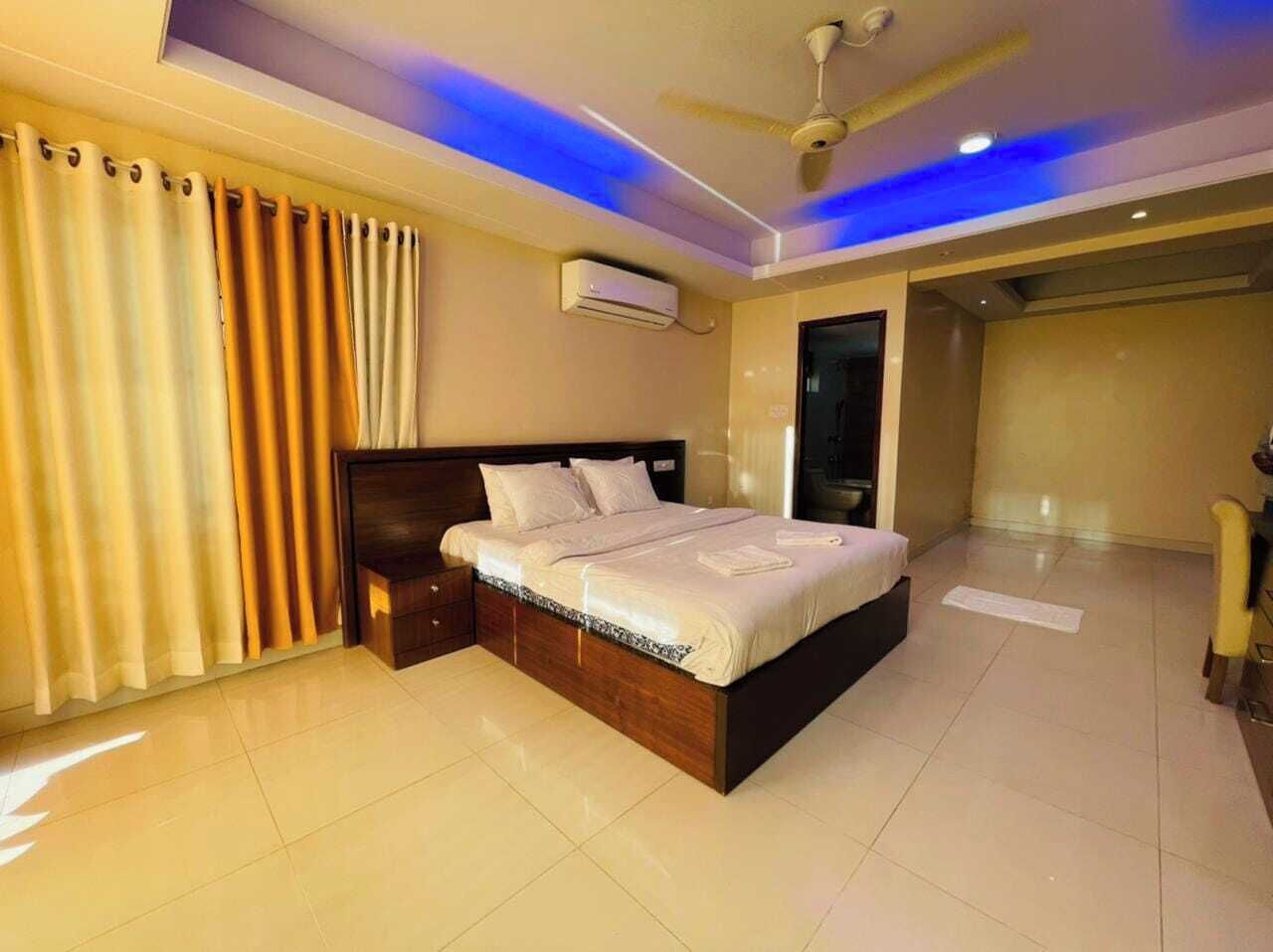 A bedroom with a bed, a ceiling fan, an air conditioning unit, and a door leading to another room.