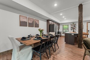 Cocina moderna con una isla central, suelo de madera y comedor con sillas y una mesa preparada para cuatro personas.