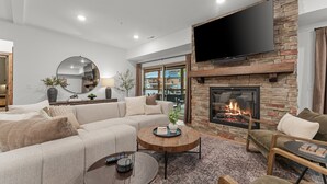 Un salon moderne avec une cheminée en pierre, un grand téléviseur à écran plat et des sièges confortables.