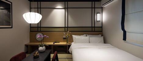 Una habitación de hotel con cama, mesita de noche, escritorio, silla y una lámpara colgante.