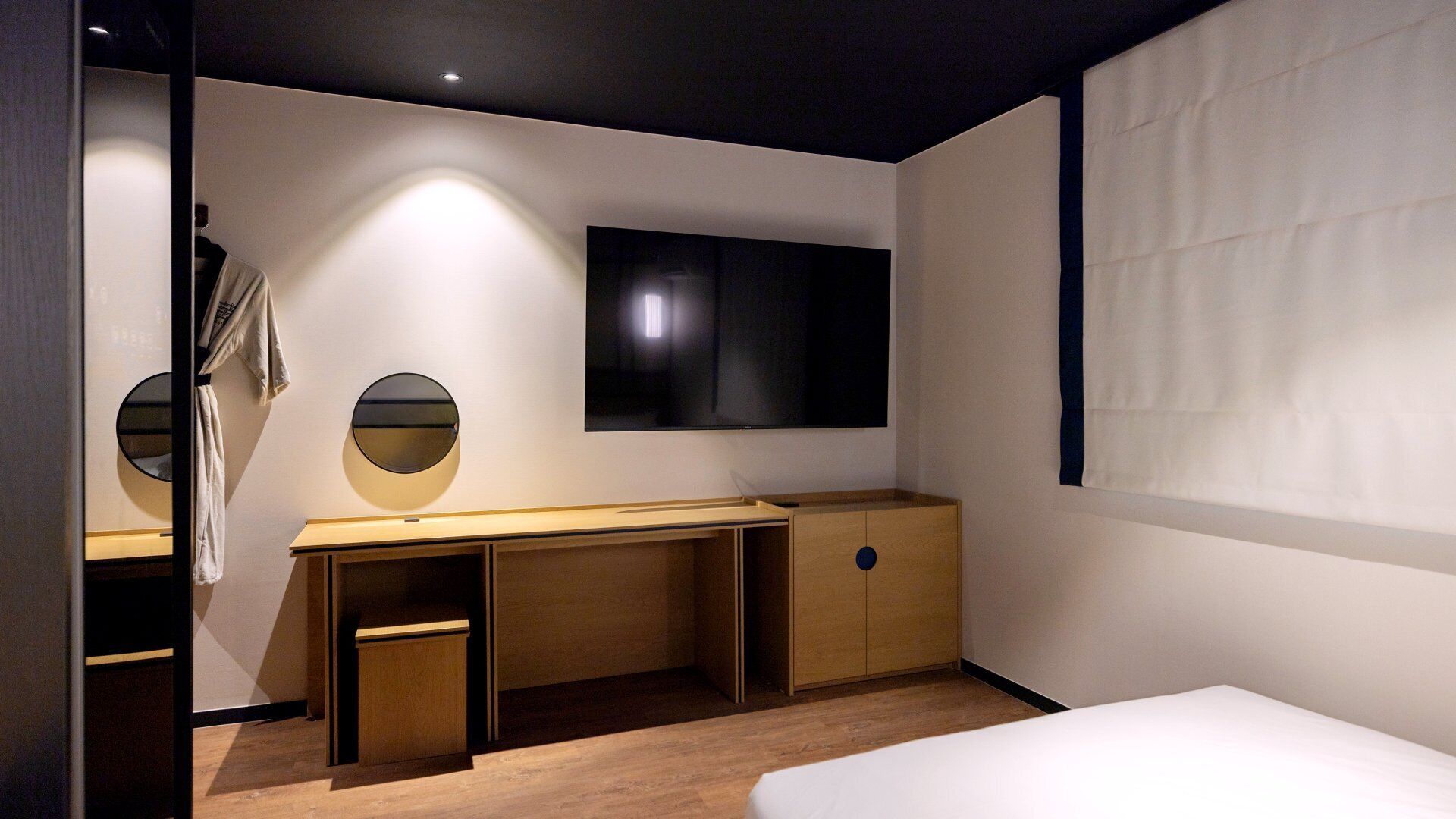 A modern bedroom with a bed, a desk, and a TV mounted on the wall.