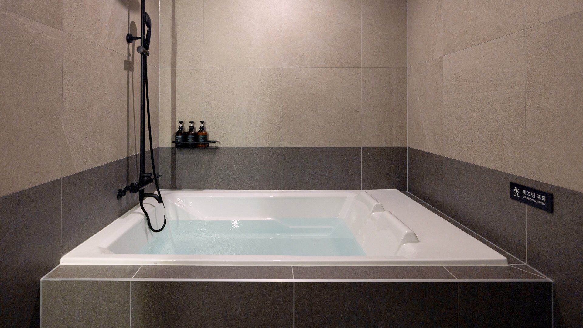 Et moderne badeværelse med badekar, brusehoved og en hylde med toiletartikler.