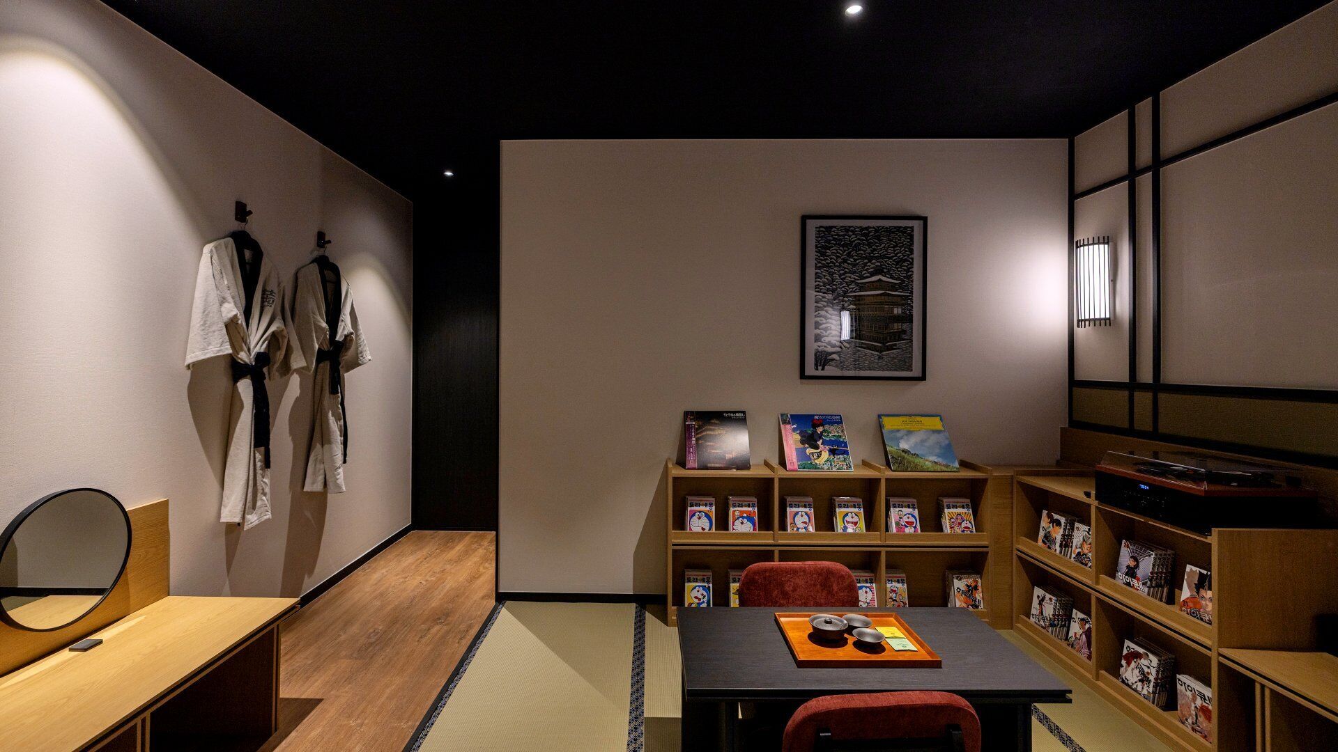 A room with a wooden floor, a table with a tray, a bookshelf with books, and a framed picture on the wall.