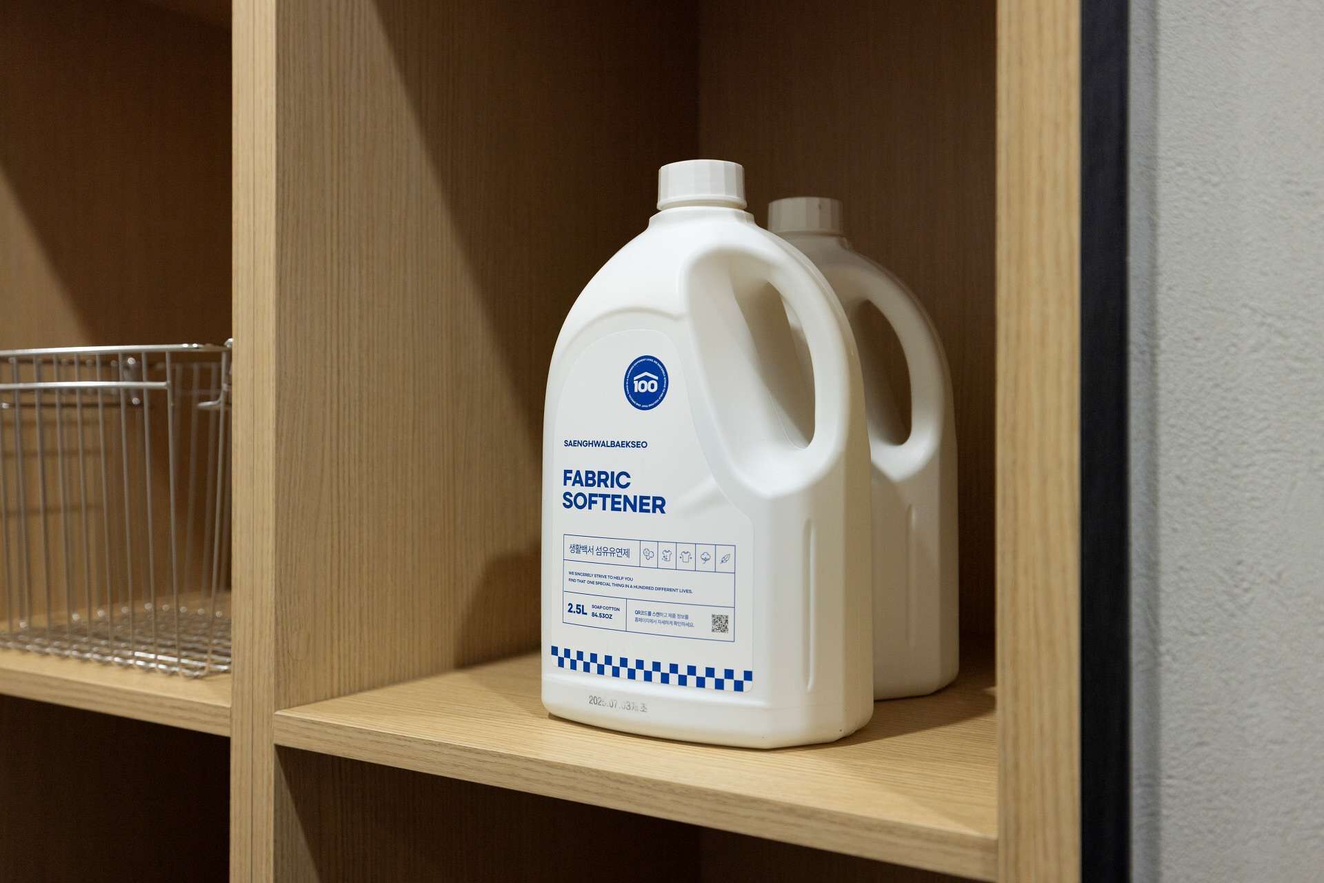 A white plastic container labeled 'FABRIC SOFTENER' on a wooden shelf.